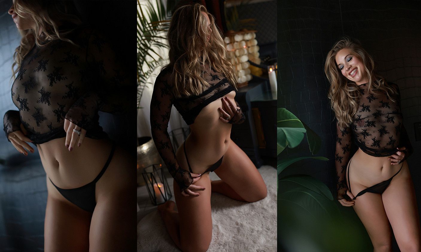 Woman in black lace lingerie posing in moody dark studio lighting, showcasing elegant sheer bodysuit design.