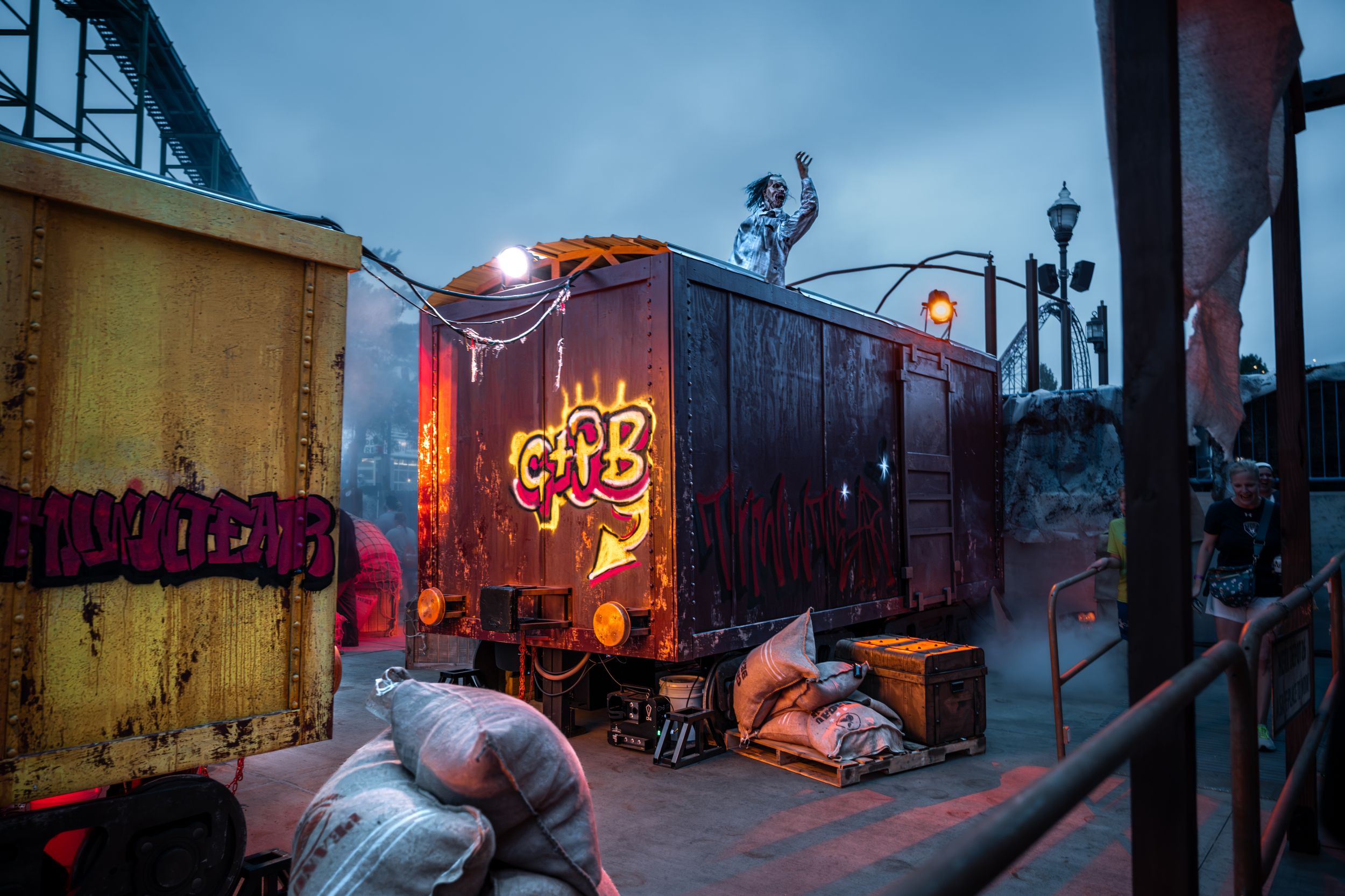 A dark, atmospheric scene featuring a vintage freight train car with graffiti at dusk, surrounded by eerie carnival decorations.