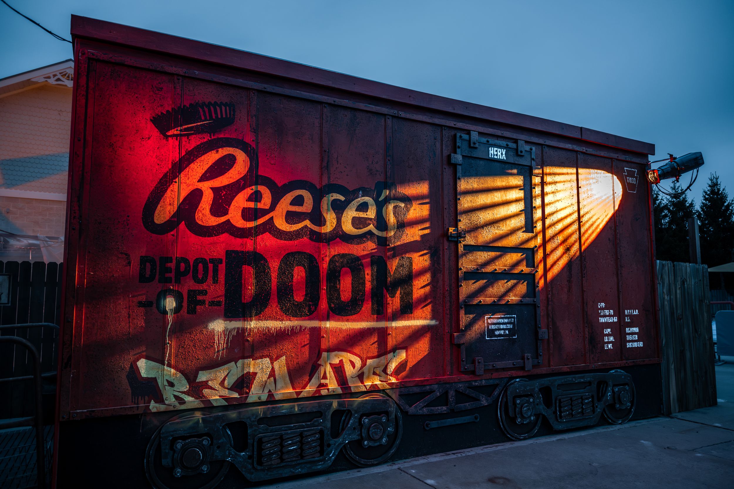 A vintage red train car painted with the Reese's Depot of Doom logo and graffiti art at dusk.