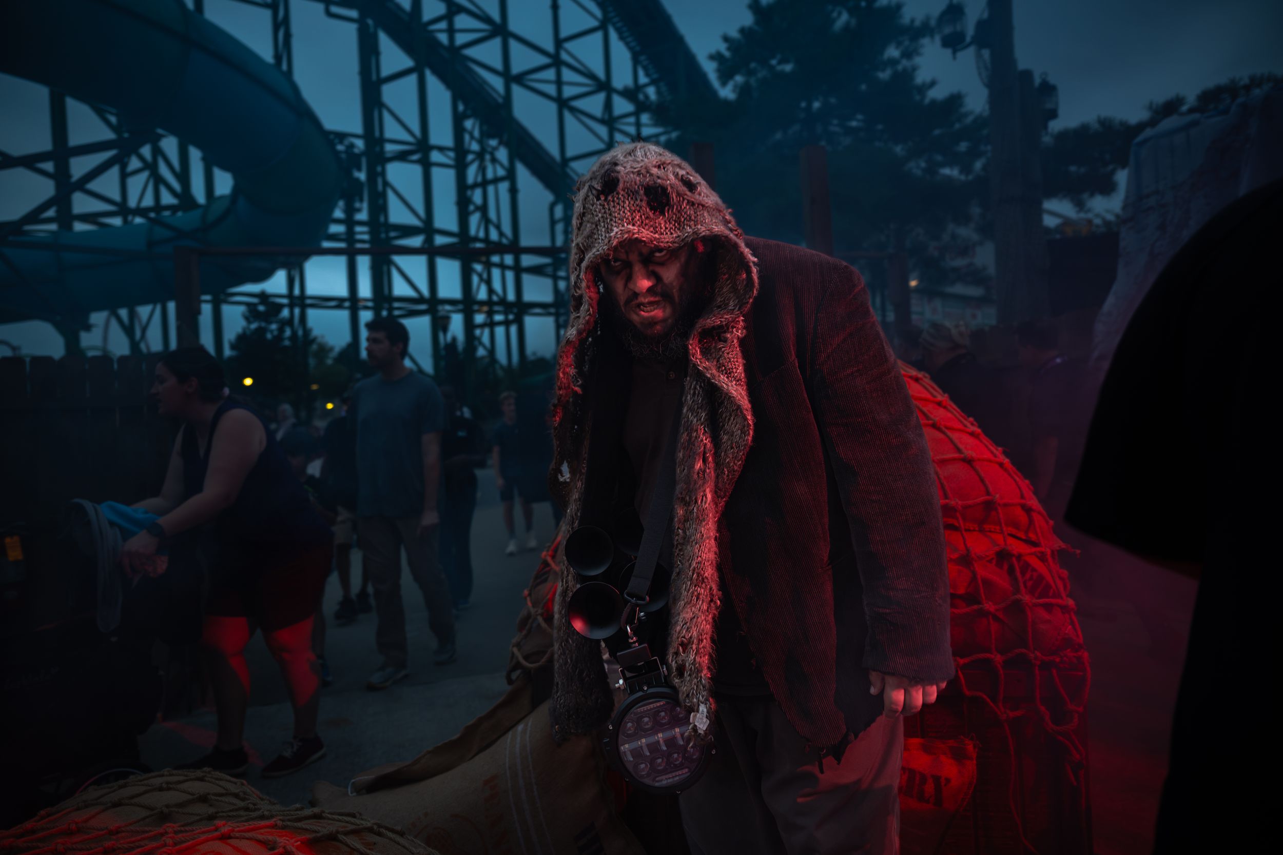 Scary Halloween horror actor in bloody costume poses at dark amusement park haunted attraction event.