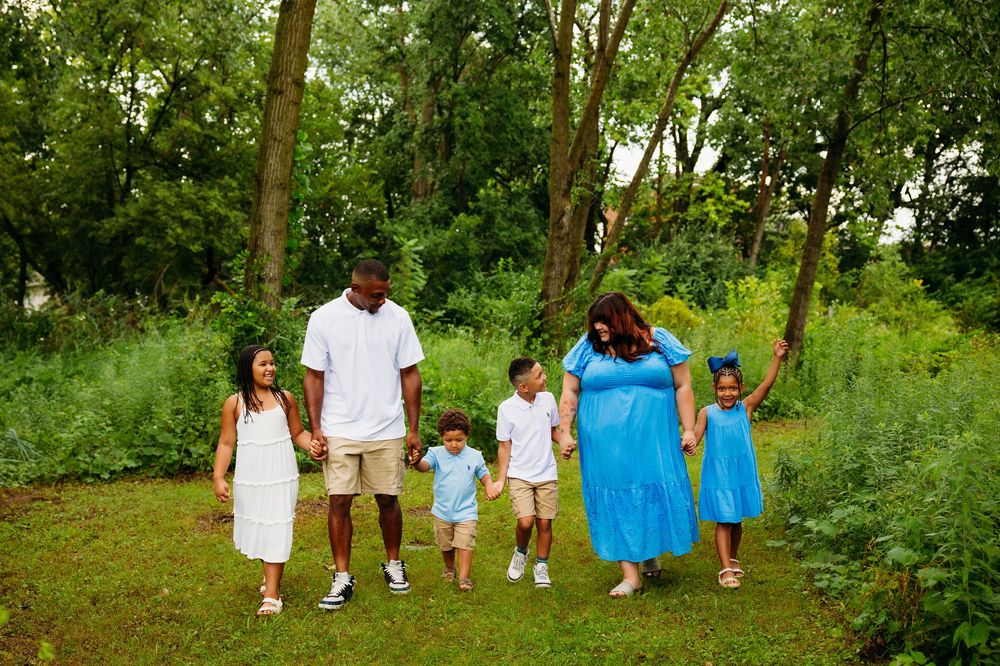 Happy family of six walking hand in hand through a green wooded park.