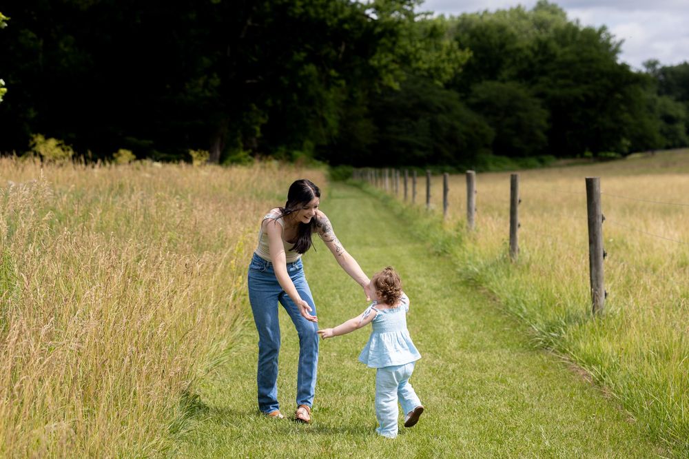 Mother and young daughter holding hands while walking along a scenic grassy path outdoors.