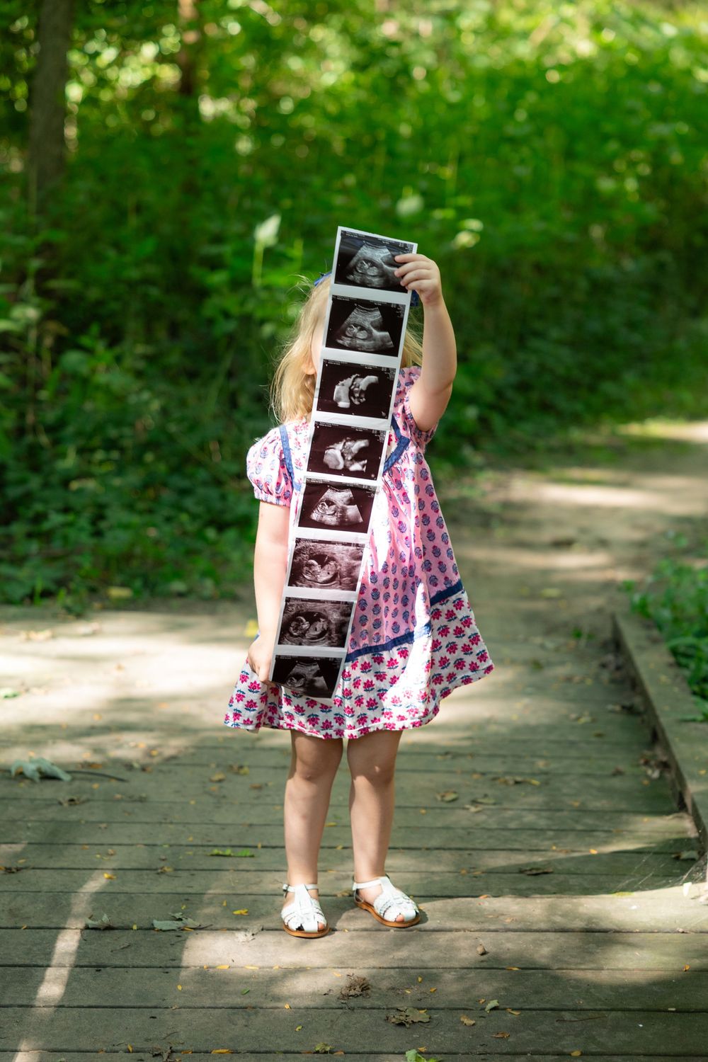 Young girl holding ultrasound photos in front of her face outdoors.