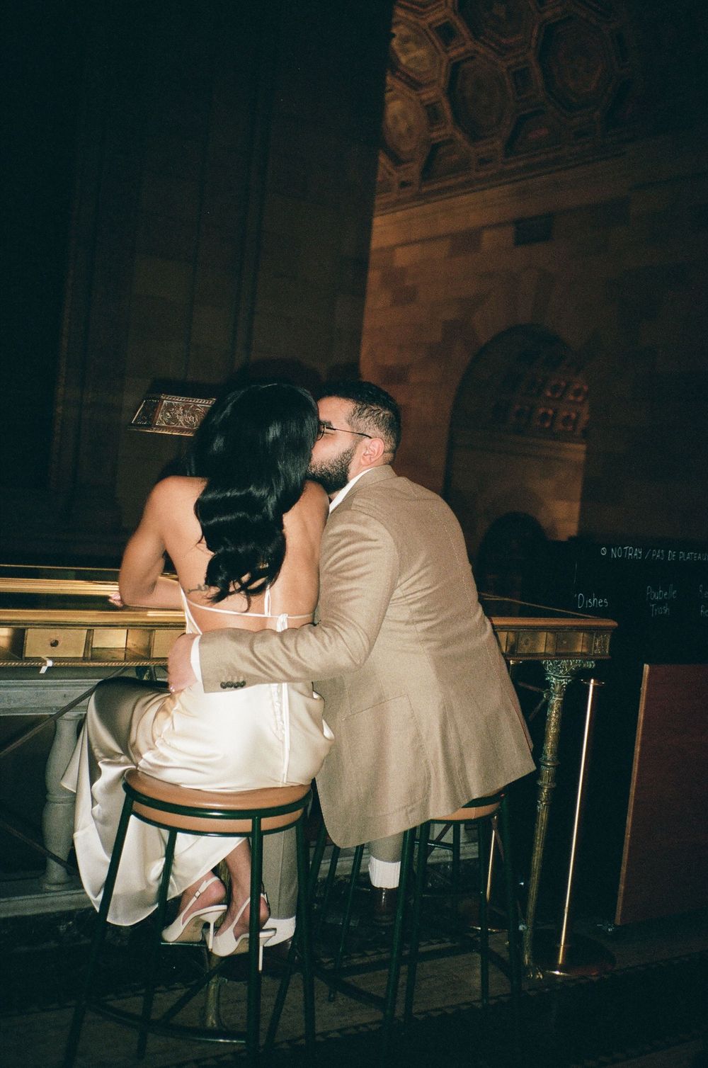 Couple sharing a romantic kiss at a bar in an elegant venue, dressed in wedding attire.