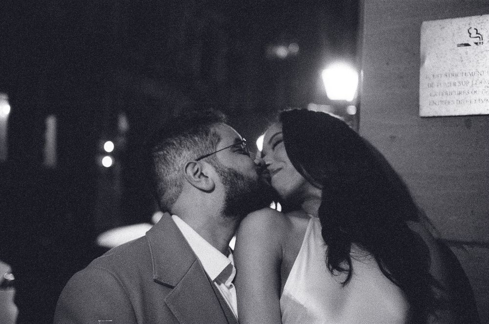 Black and white photo of a couple sharing a romantic kiss at night on a city street.