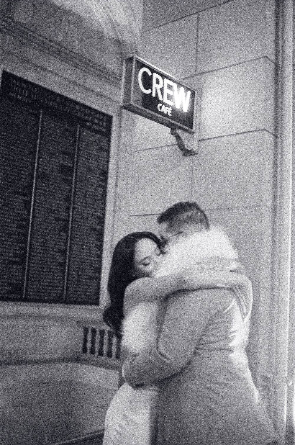 A couple shares a romantic embrace outside Crew Café in a black and white film photograph.