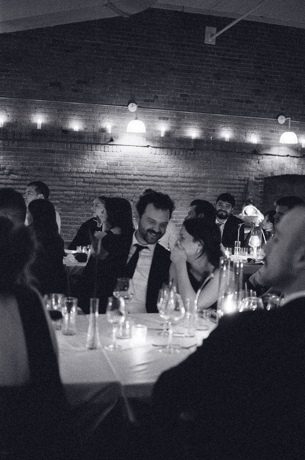 Black and white photo of a couple sharing a joyful moment at a candlelit wedding reception dinner table.