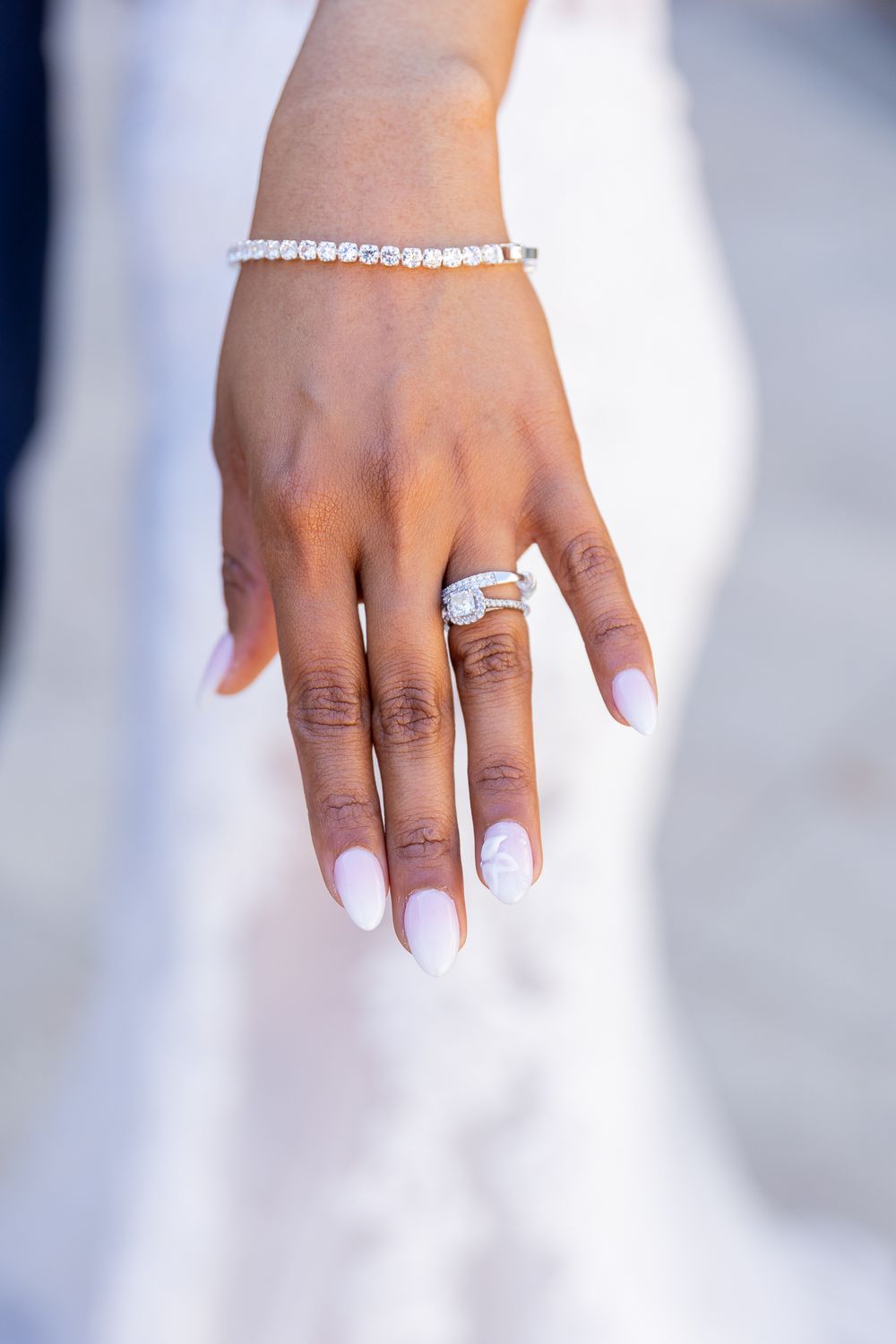 Close-up of a bride's hand displaying a diamond engagement ring and tennis bracelet with white manicured nails.