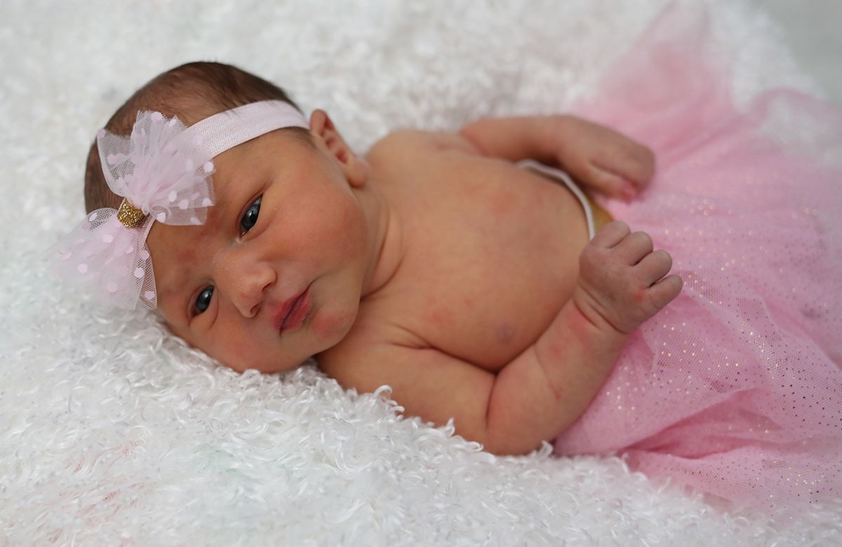 Adorable newborn baby girl lying on white fluffy blanket wearing pink tutu and floral headband.
