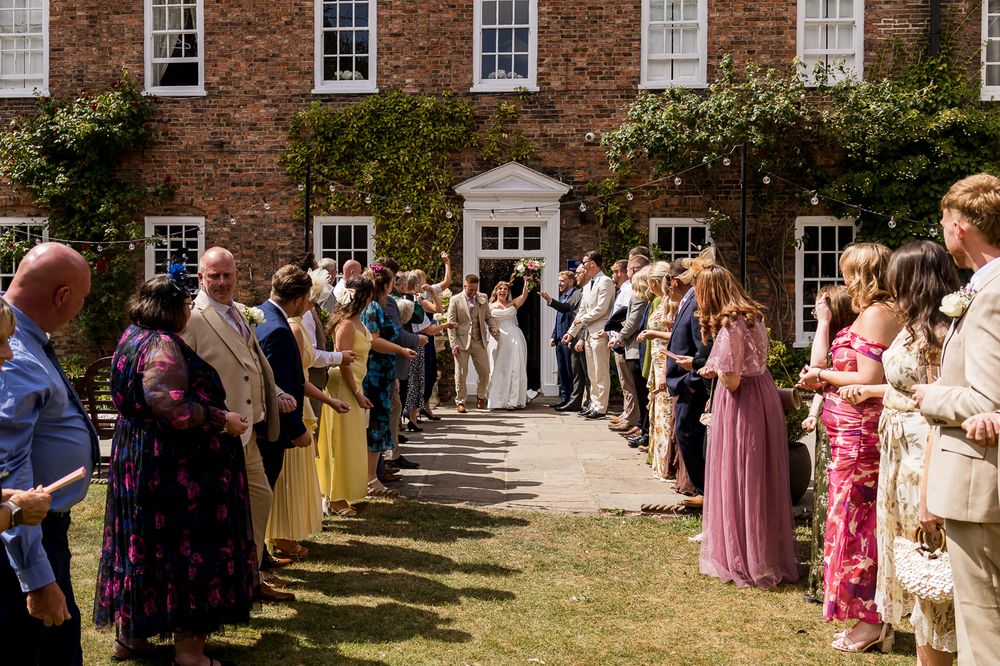 Outdoor wedding ceremony at a brick manor house, guests lining the aisle as couple stands at the altar.