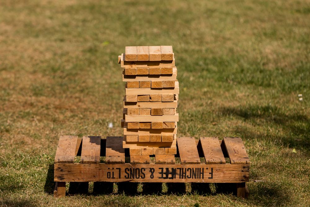 Giant Jenga tower stacked on a wooden crate outdoors on green grass at a garden party event.