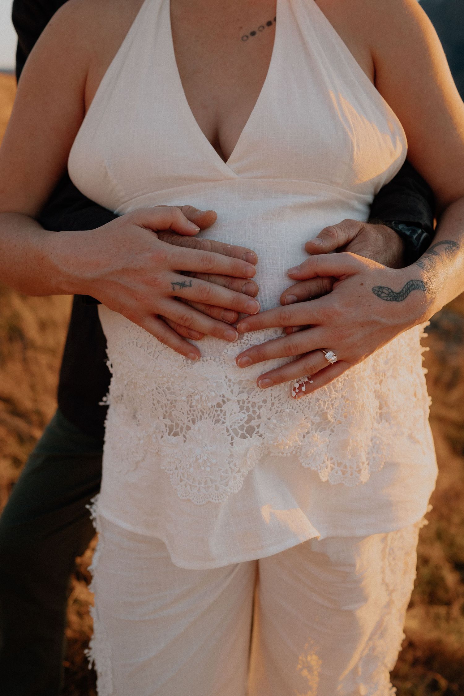 Man proposing on one knee to woman by a mountain lake at golden hour sunset in grassy field.