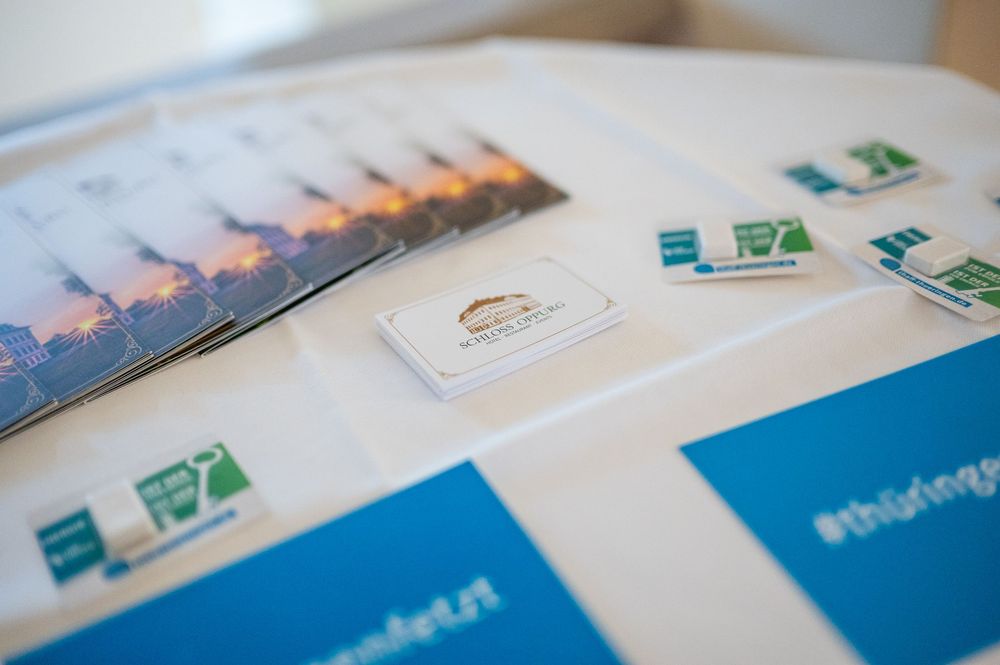 Brochures with sunset cityscape covers, business cards, and small green and white cards arranged on a table with blue event signage.