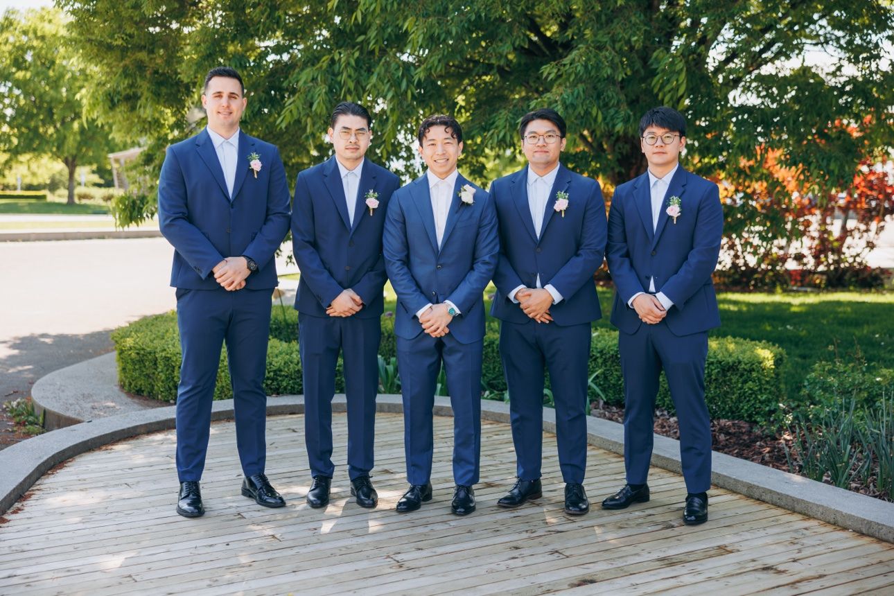 Groom and his groomsmen in navy suits outside Celebration Pavilion at Queen Elizabeth Park