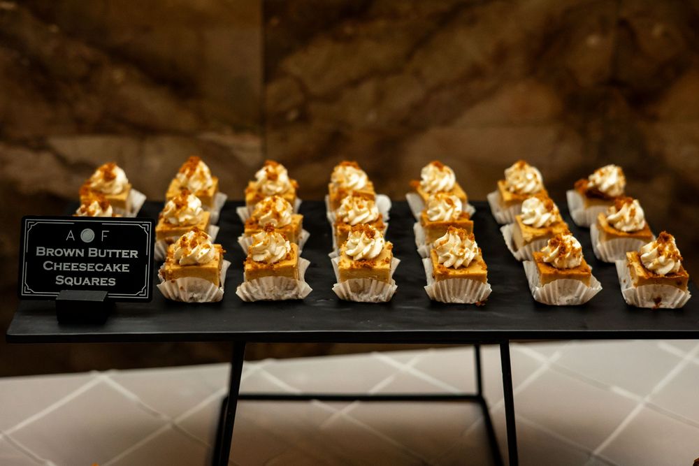 Rows of Brown Butter Cheesecake Squares with golden caramel topping displayed on a black serving tray.