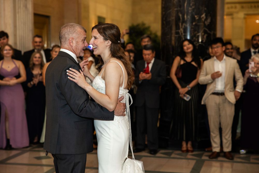 Bride and groom share their first dance at elegant wedding reception with guests watching in formal attire.