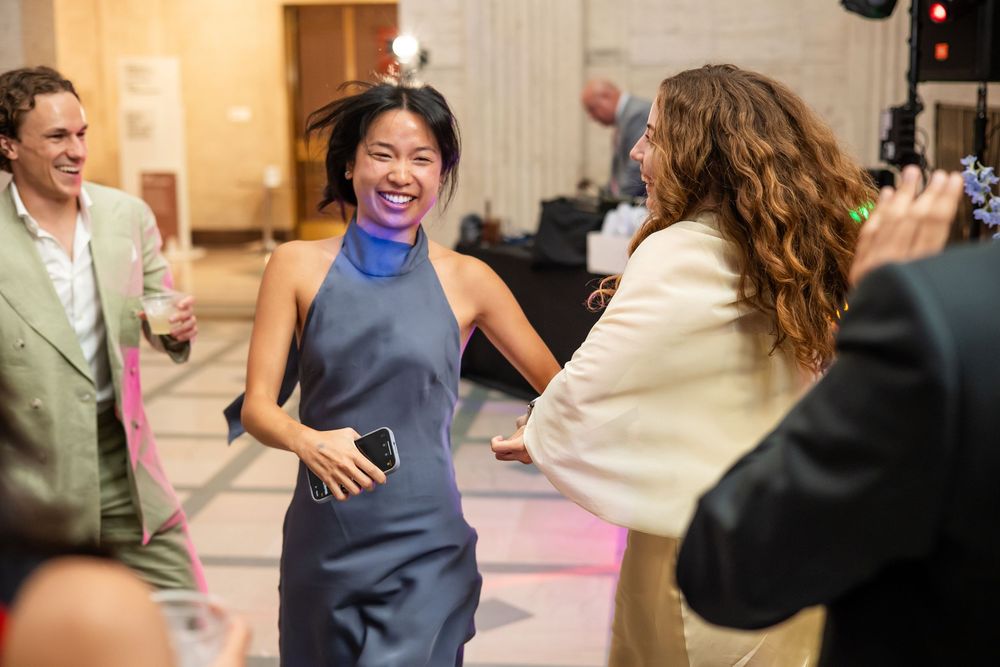 Woman in blue halter dress laughing and dancing with guests at an elegant indoor celebration event.