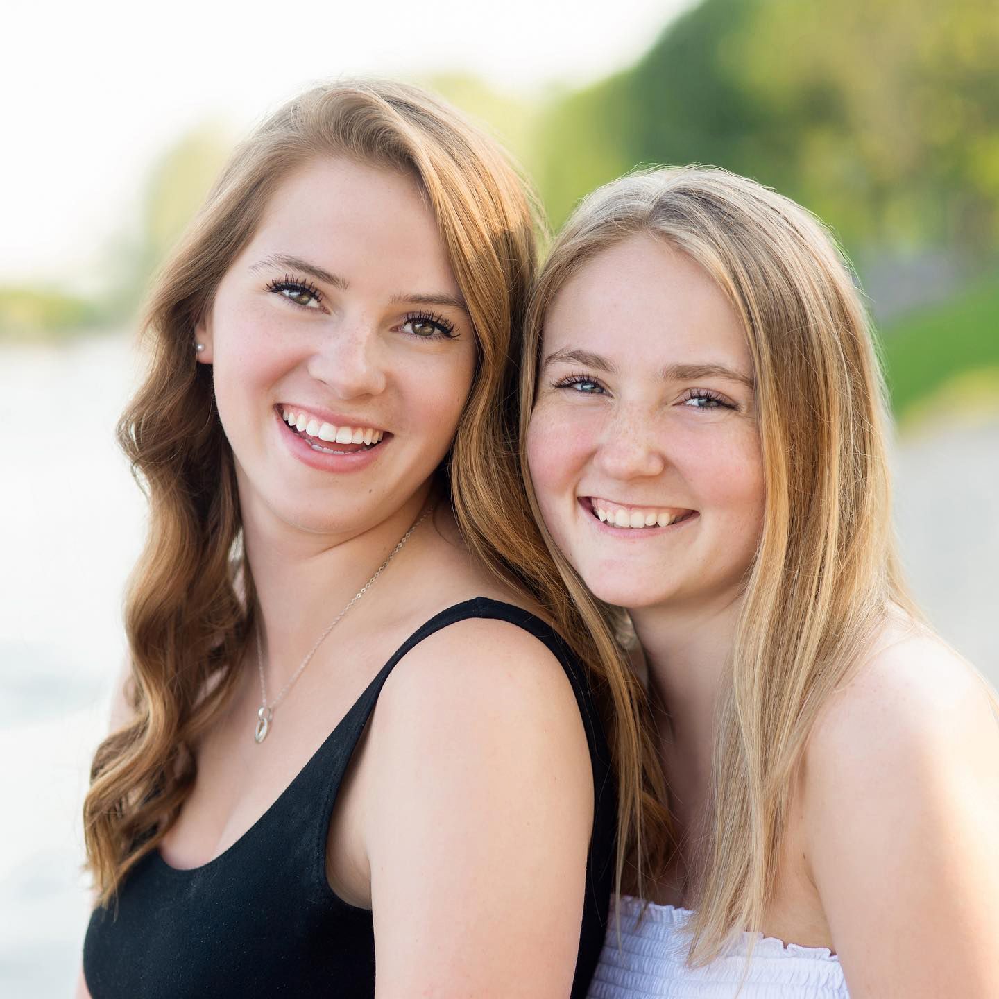 Two smiling teenage girls posing together outdoors near water for senior portrait photography.