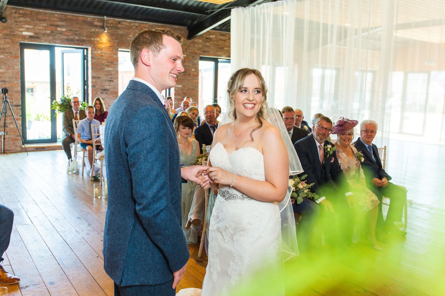 Bride and groom exchanging vows at an indoor wedding ceremony with guests seated in the background.