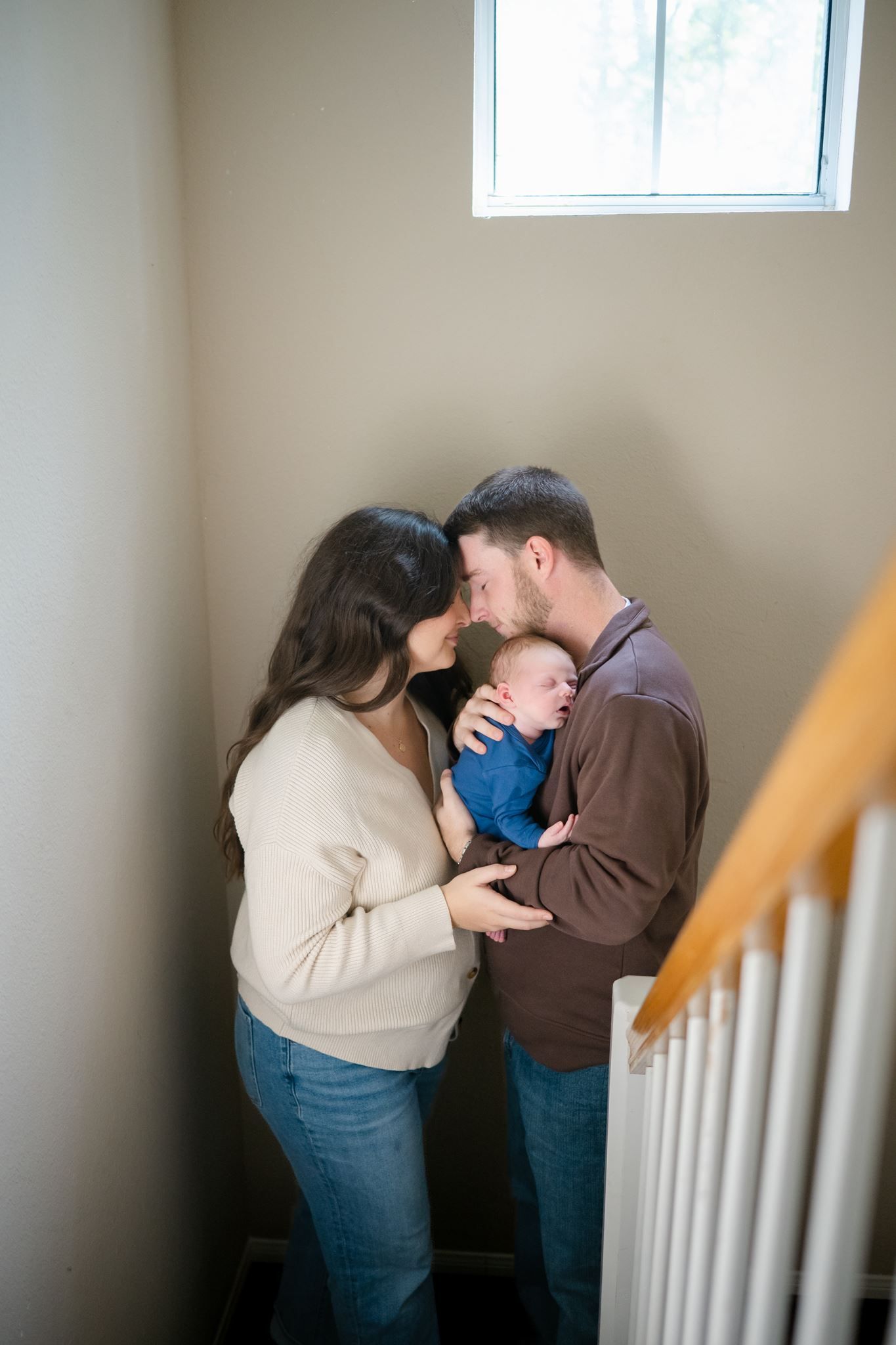 A mom and dad holding their newborn son in the stairwell of their home.
