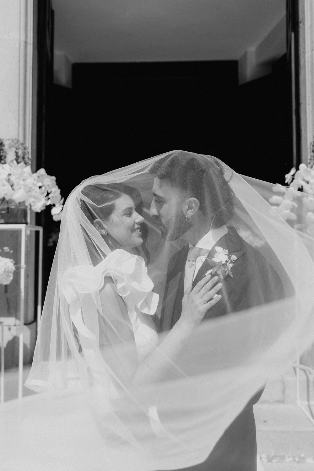 Lorenzo e Laura si baciano vicino al velo, in una fotografia in bianco e nero.
