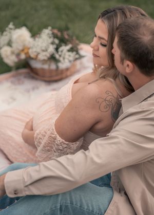 A couple shares an intimate moment on a blanket outdoors, with the woman's floral tattoo visible on her back.