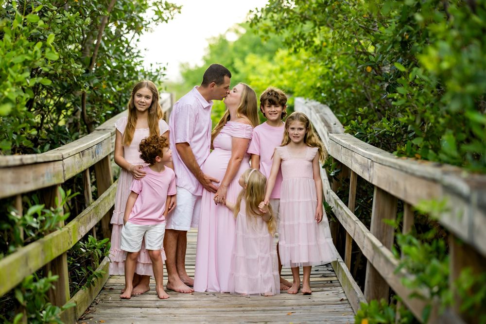 Family in matching pink outfits posing on a wooden boardwalk surrounded by lush green trees.