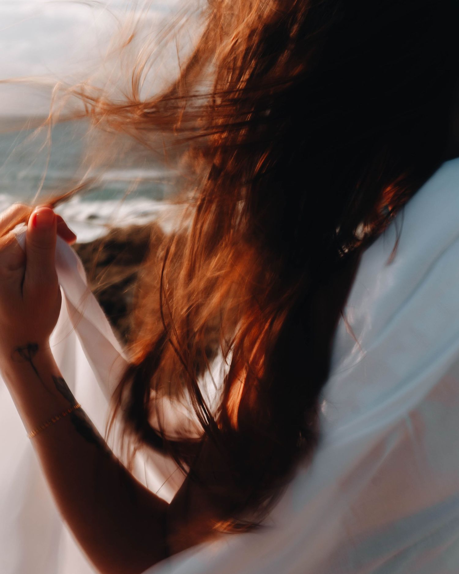 Woman with brown hair blowing in the wind, holding white fabric near a Newcastle coastal backdrop on a portrait shoot.