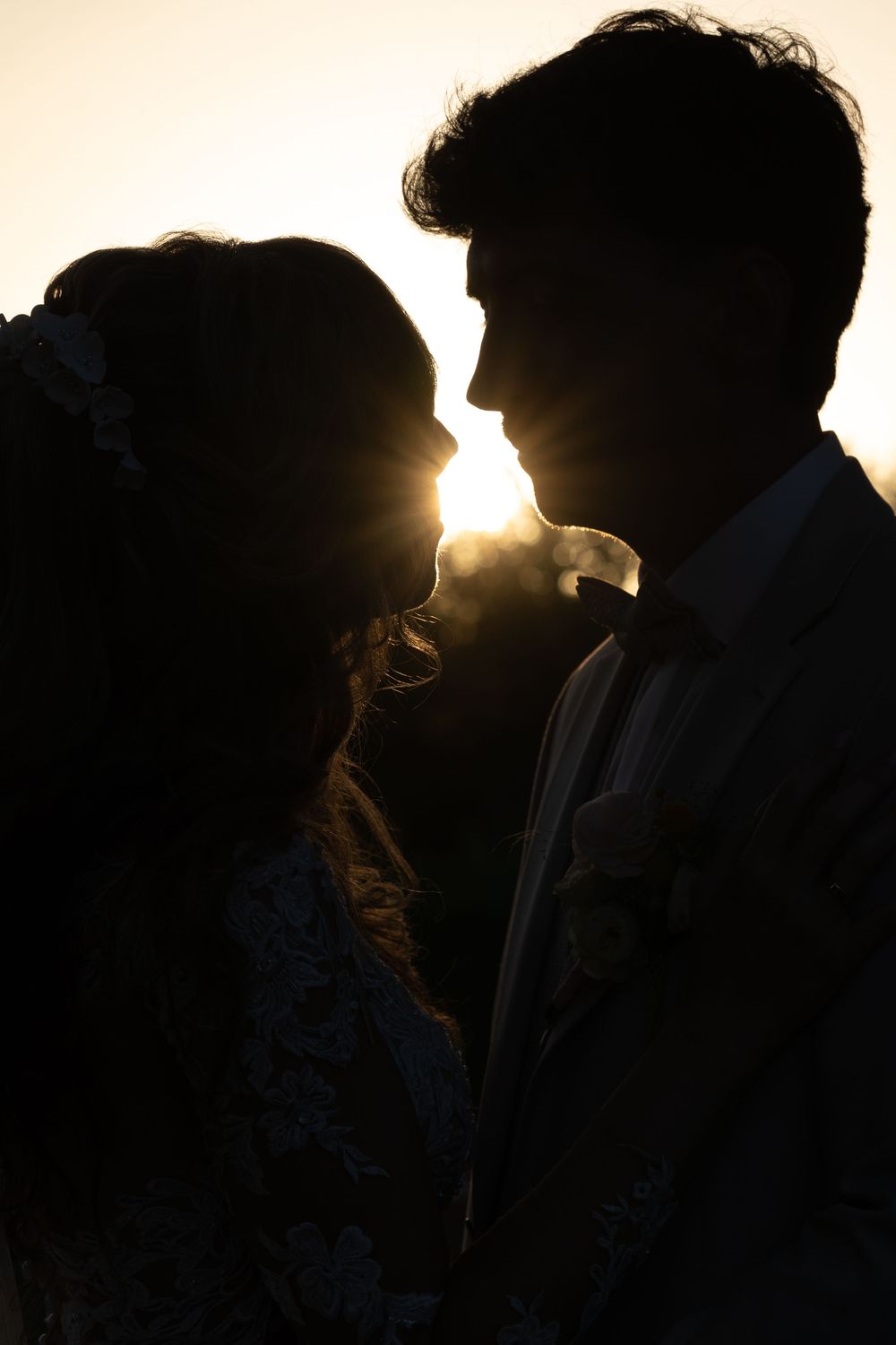 Silhouette of a bride and groom facing each other at sunset, with golden backlight glowing between them.