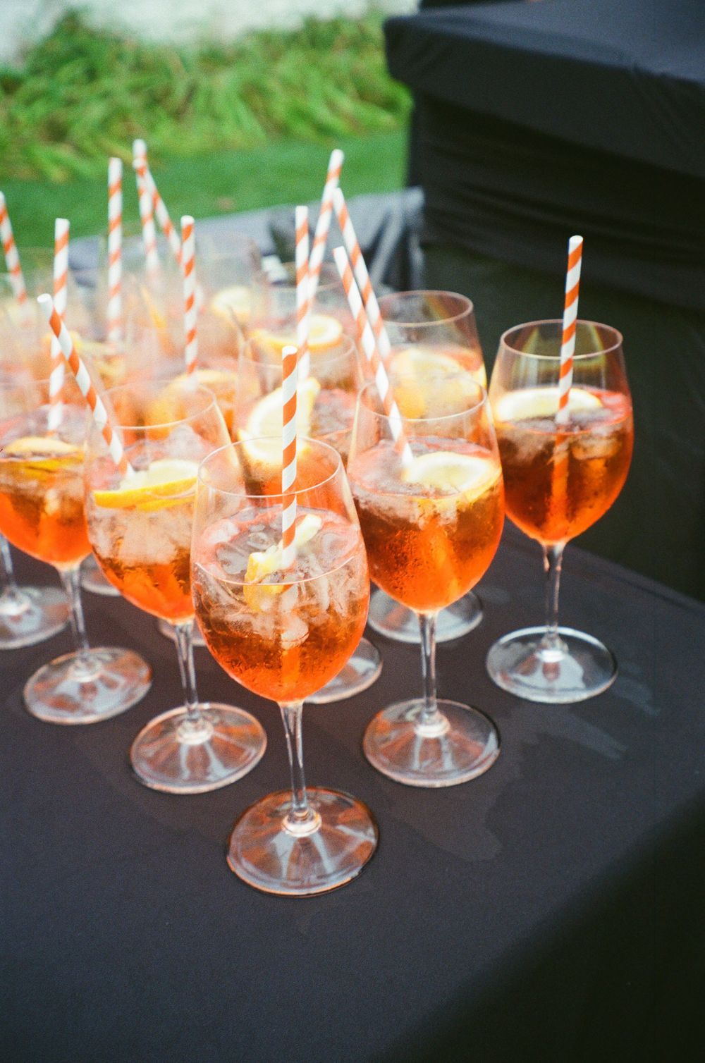 Elegant Aperol Spritz cocktails in wine glasses with orange striped straws and citrus slices on a black tablecloth.