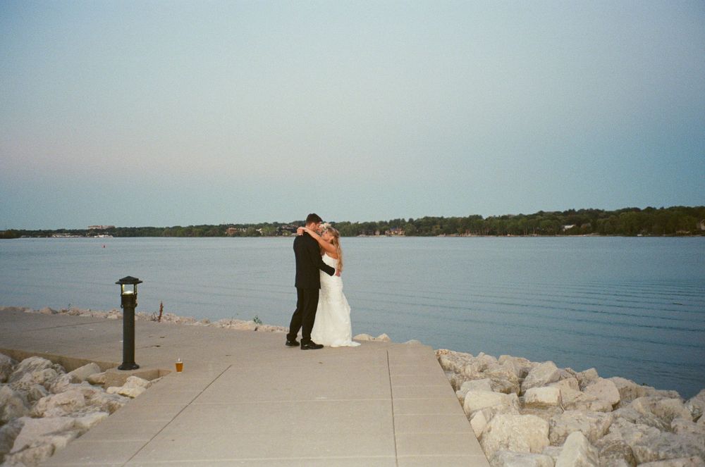Bride and groom share a romantic embrace on a waterfront pier at sunset during their outdoor wedding ceremony.