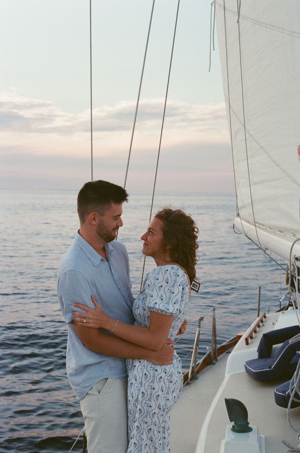 Couple embracing romantically on a sailboat deck at sunset over calm ocean waters.