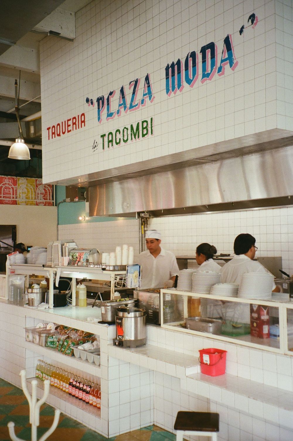 Interior of Taqueria Peaza Moda by Tacombi, featuring white tiled walls and staff working behind the counter.