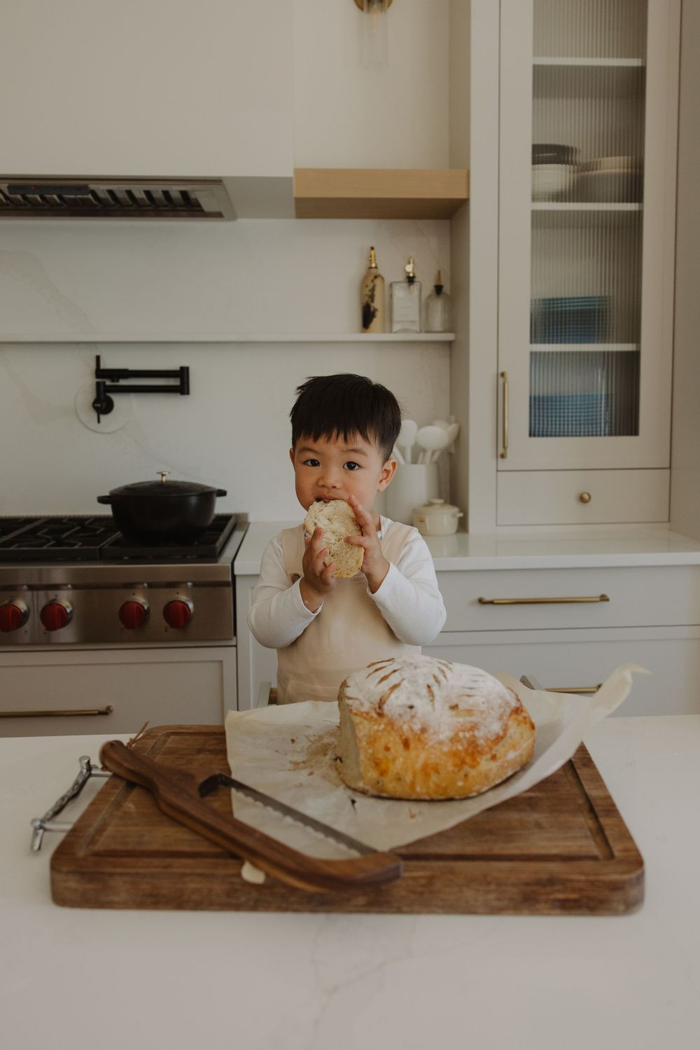 Toddler eating a piece of freshly baked bread at a kitchen counter with a rustic wooden cutting board.