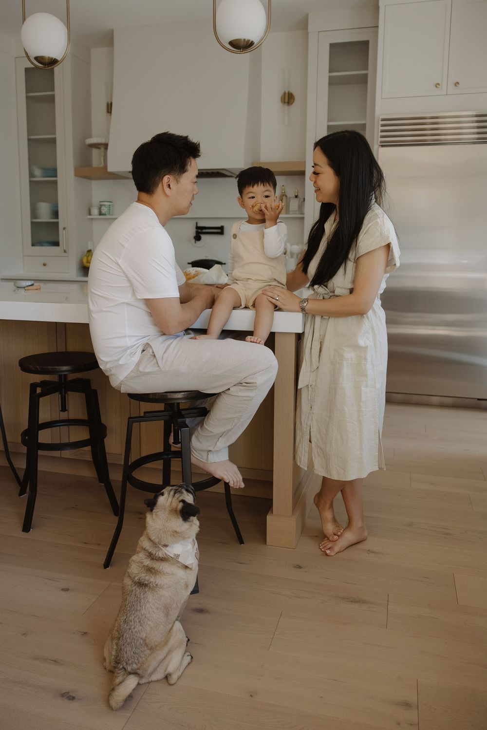 a family with toddler and dog gathered in modern white kitchen while they get thier picture taken for family photos in Central Alberta