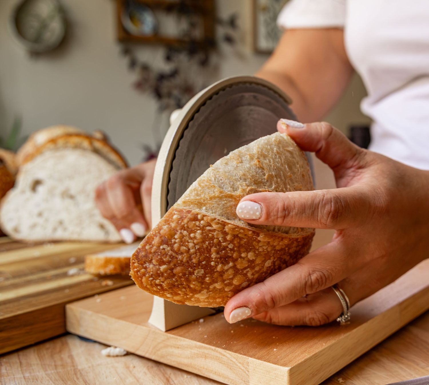Hands slicing fresh sourdough bread on a wooden cutting board with a ceramic bread slicer guide.