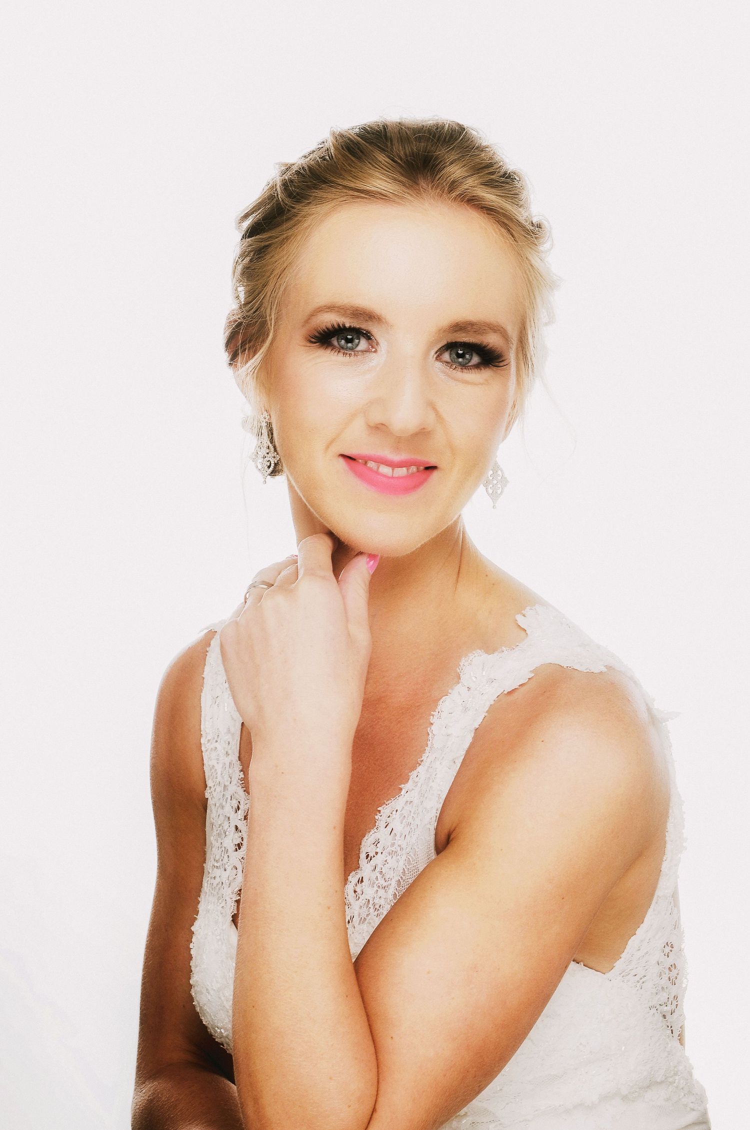 Bridal portrait in white lace dress with classic makeup and upswept hairstyle.