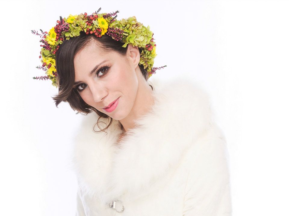 Portrait of a woman wearing a colorful floral crown and white fur wrap.