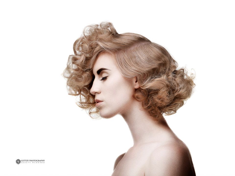 Profile studio portrait showcasing elegant curled hairstyle against white background.