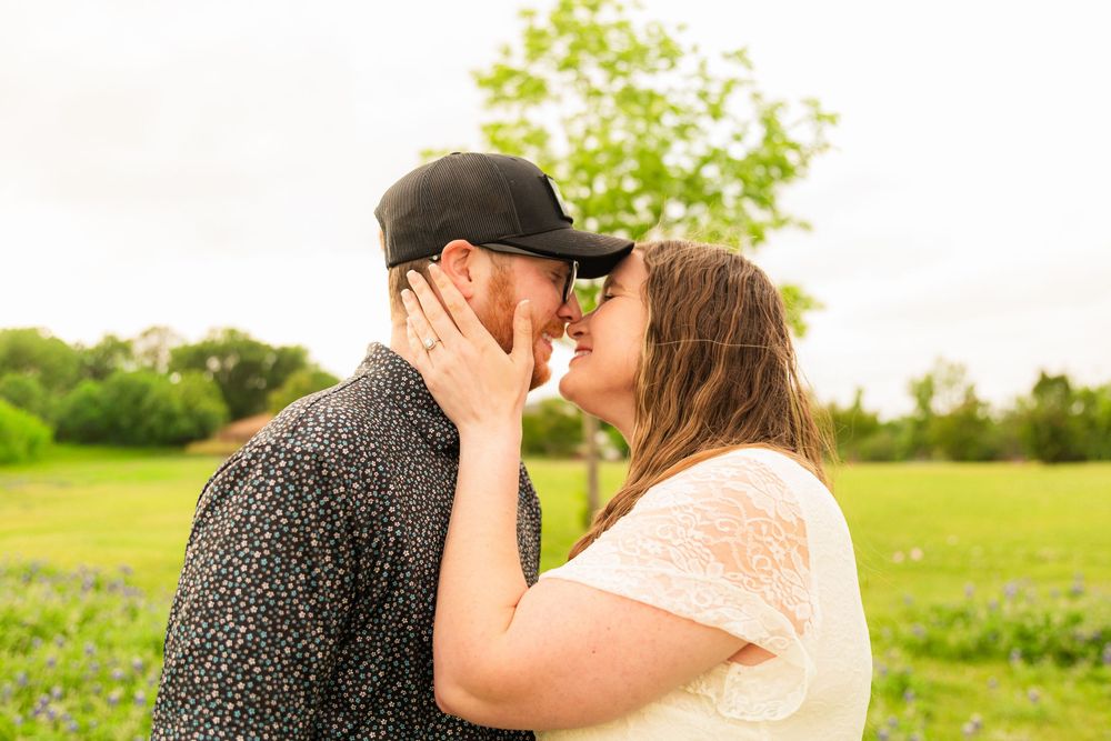 Couple sharing a romantic kiss in a lush green field, man wearing a black cap and woman in a white top.