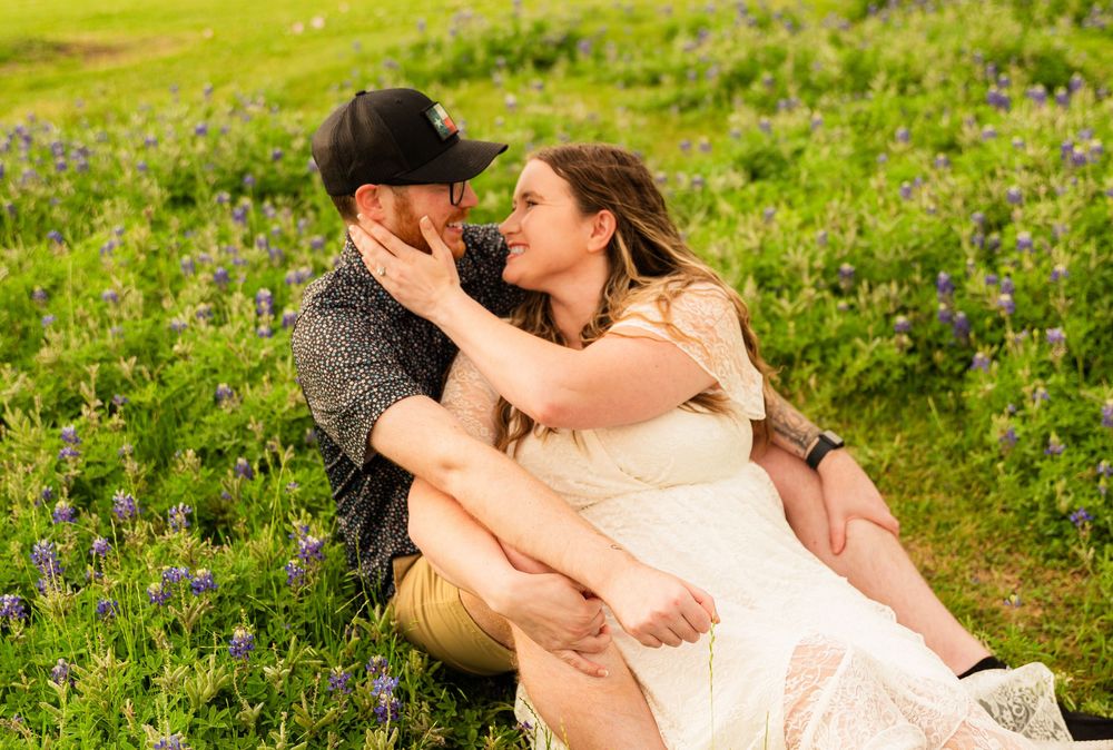 Couple sharing a romantic moment in a lush bluebonnet field, woman in white dress cradling man's face.