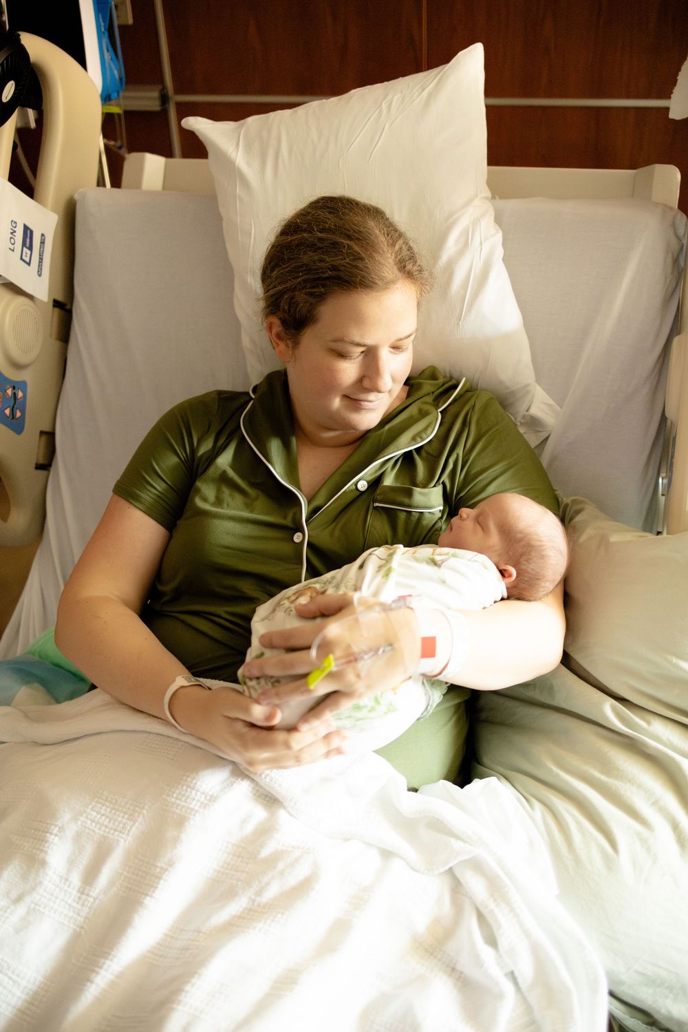 New mother holding newborn baby while resting in hospital bed after giving birth fresh 48 newborn photography at University of Tennessee.
