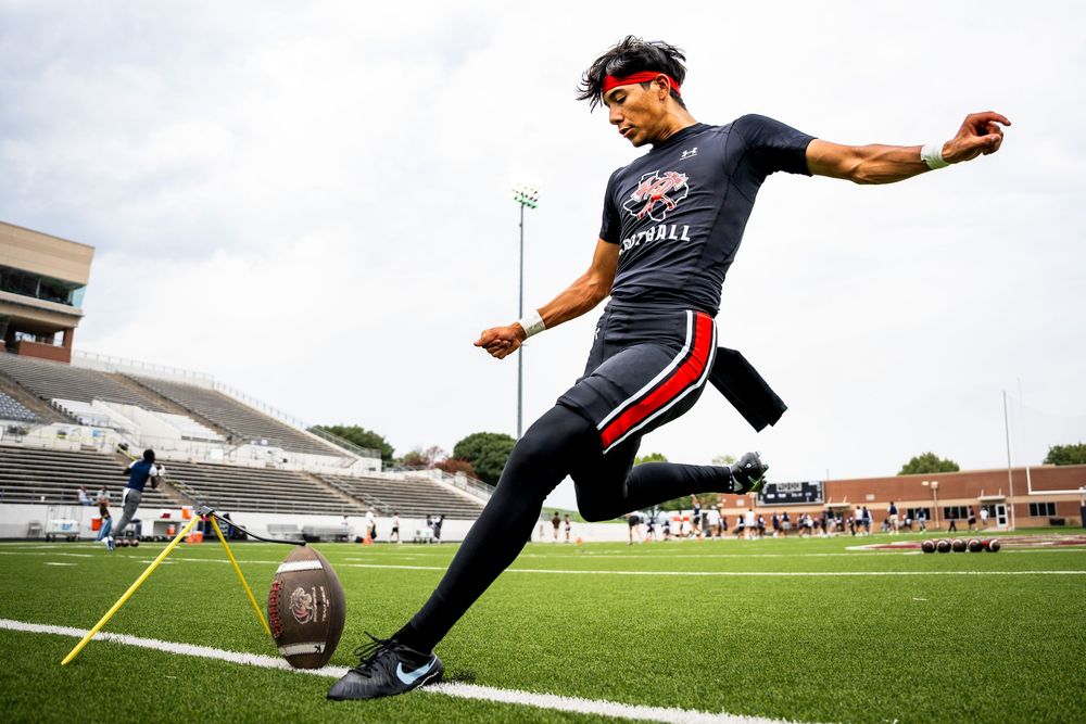 Football player practices kicking on a stadium field during an outdoor training session.