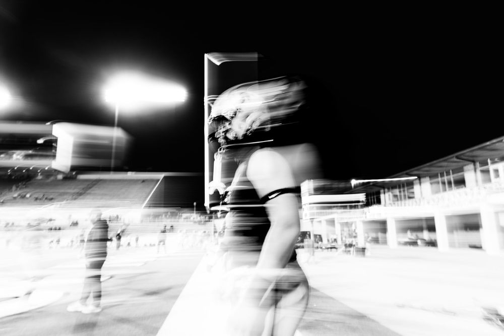 Dynamic black and white motion blur photo of an athlete running on a football field at night.