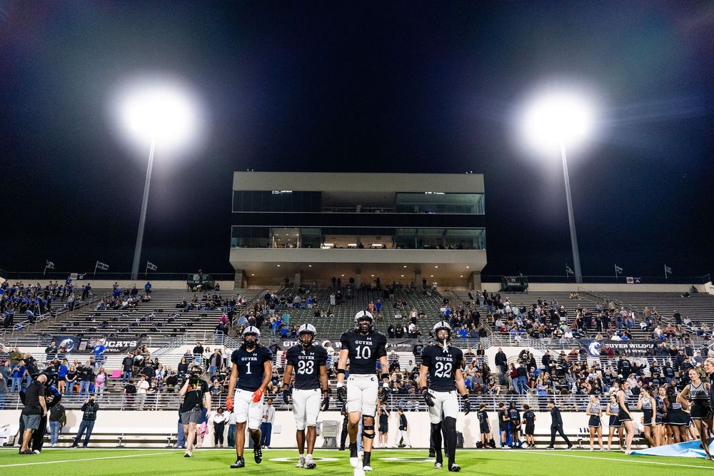 Football team standing on illuminated night game field under bright stadium lights with fans in stands.