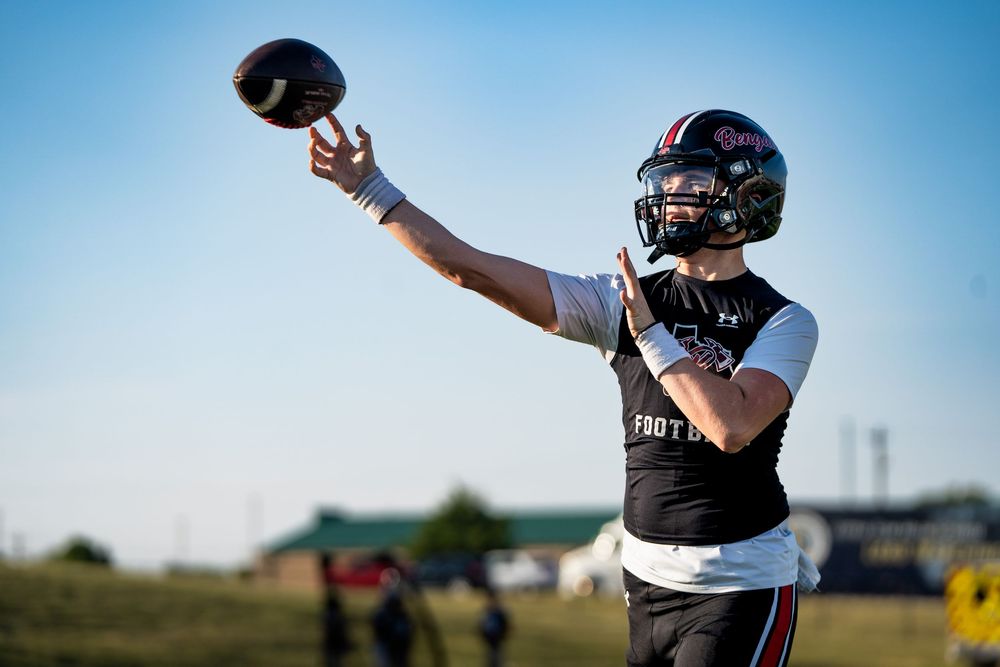 Quarterback in red practice jersey throwing a football during outdoor morning practice session.