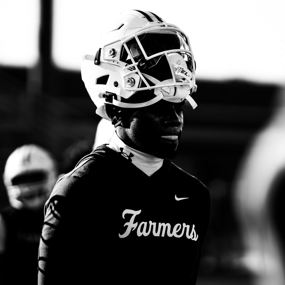 Black and white portrait of a football player wearing a Farmers team helmet during practice.