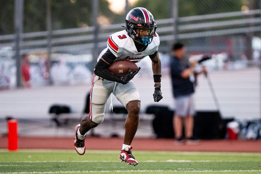 Football player in red and white uniform runs with the ball during a stadium game.