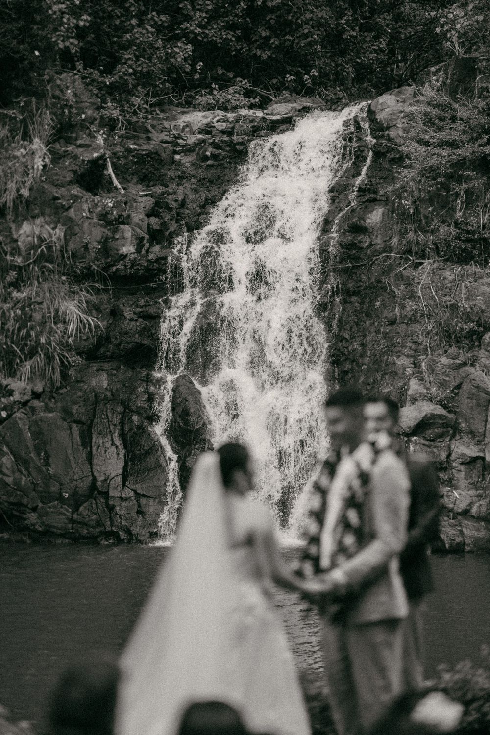 Black and white photo of a couple exchanging vows before a stunning waterfall during their Hawaii wedding.