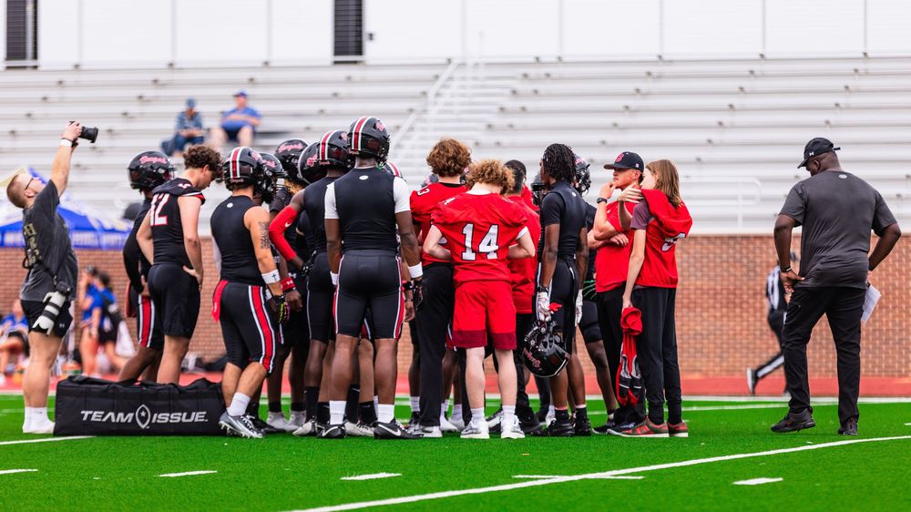 High school football team huddles together on field during a daytime practice or game.